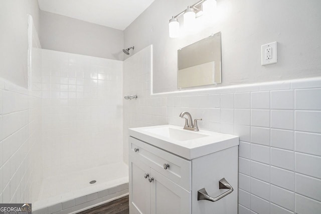 bathroom with tiled shower, vanity, hardwood / wood-style flooring, and tile walls