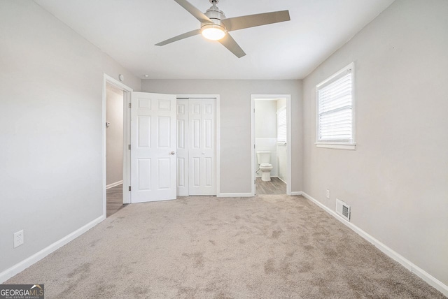 unfurnished bedroom with light colored carpet, ensuite bath, and ceiling fan