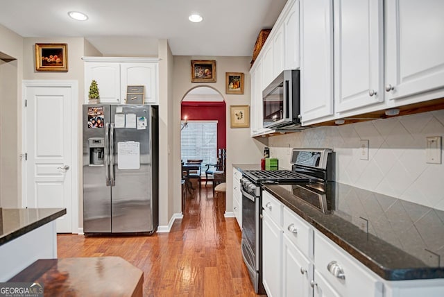 kitchen featuring white cabinetry, tasteful backsplash, dark stone counters, appliances with stainless steel finishes, and light wood-type flooring