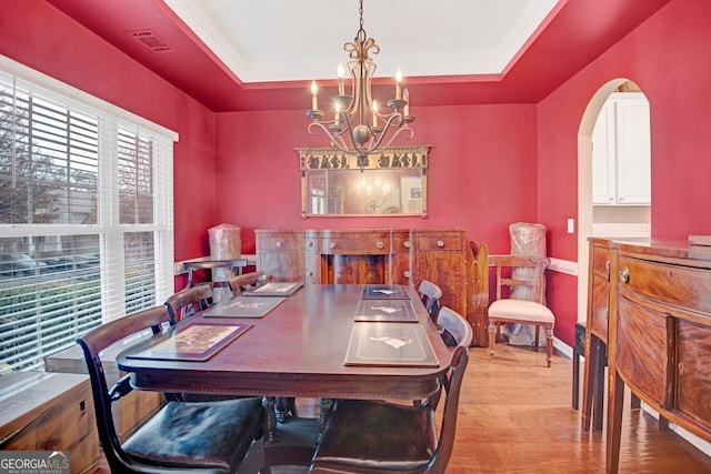 dining room with a notable chandelier, light hardwood / wood-style floors, and a raised ceiling