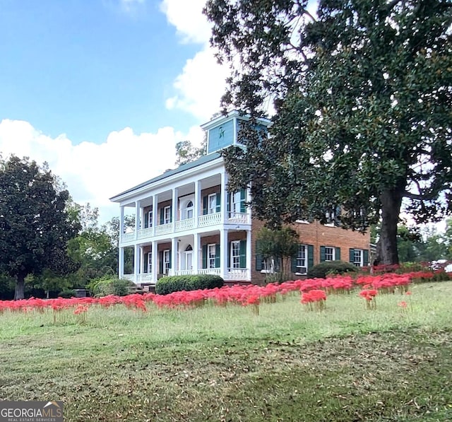 view of front facade with covered porch, a balcony, and a front lawn