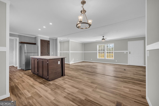 kitchen with stainless steel refrigerator, crown molding, dark brown cabinetry, and ceiling fan with notable chandelier