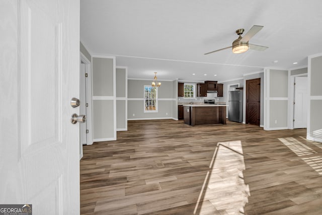 unfurnished living room with hardwood / wood-style floors, ceiling fan with notable chandelier, and ornamental molding