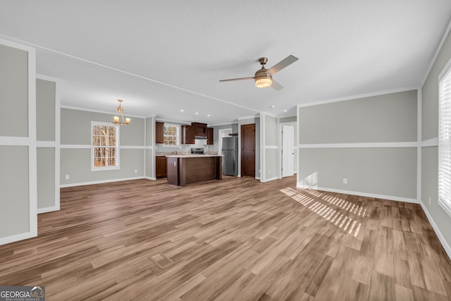 unfurnished living room featuring ceiling fan with notable chandelier, light wood-type flooring, and ornamental molding