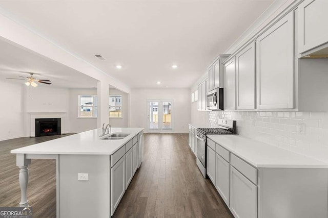 kitchen featuring sink, ceiling fan, an island with sink, decorative backsplash, and appliances with stainless steel finishes