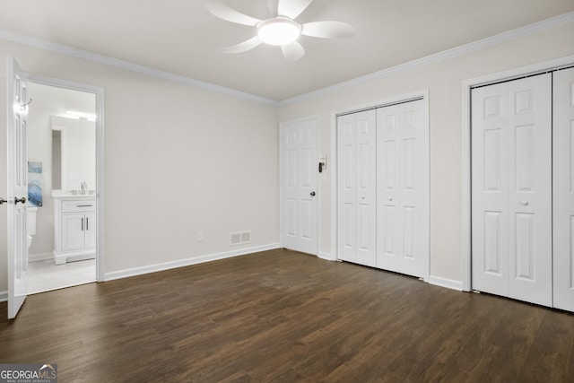 unfurnished bedroom featuring ensuite bathroom, crown molding, ceiling fan, dark hardwood / wood-style floors, and multiple closets