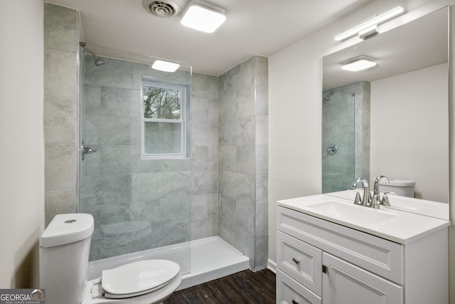 bathroom with a tile shower, vanity, toilet, and hardwood / wood-style floors