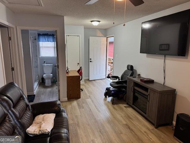 living room with ceiling fan, a textured ceiling, and light hardwood / wood-style flooring