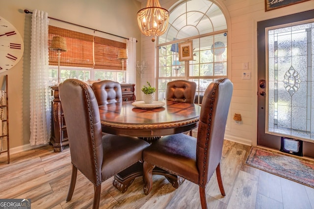 dining area featuring light wood-type flooring, wooden walls, and a chandelier