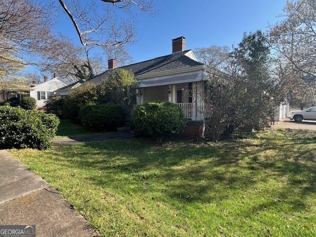 view of side of home featuring a porch, a chimney, and a yard