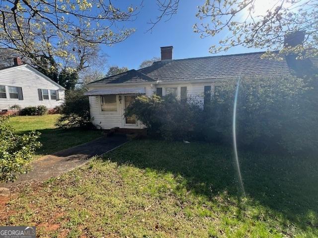 back of house featuring a lawn and a chimney