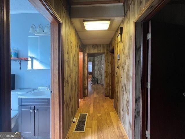hallway with light wood finished floors, visible vents, wood walls, and a sink