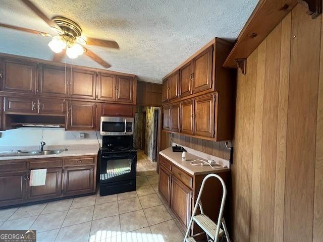 kitchen with a sink, stainless steel microwave, ceiling fan, light countertops, and range