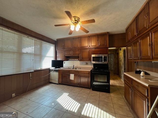 kitchen featuring dishwasher, light tile patterned floors, stainless steel microwave, a sink, and black electric range