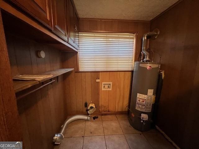 laundry room featuring wood walls, a textured ceiling, gas water heater, and light tile patterned floors