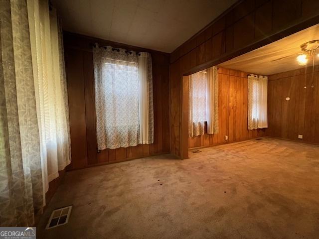 spare room featuring wooden walls, visible vents, and carpet