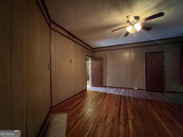 unfurnished living room with a textured ceiling, a ceiling fan, crown molding, hardwood / wood-style floors, and wooden walls