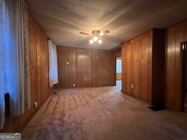 empty room with light colored carpet, wood walls, and a ceiling fan