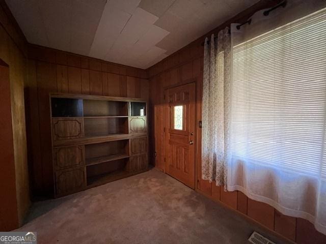entrance foyer with carpet, visible vents, and wood walls