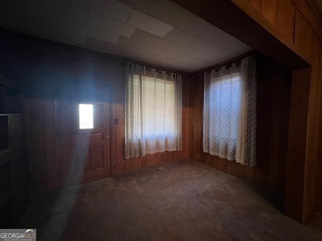 empty room featuring wooden walls, carpet, and visible vents