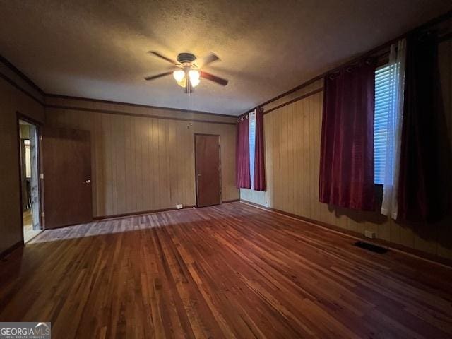 unfurnished living room featuring a ceiling fan, wood finished floors, a textured ceiling, wood walls, and visible vents