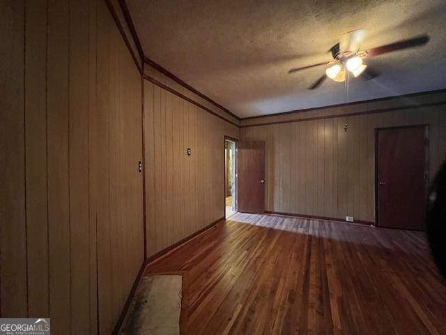 unfurnished living room with a textured ceiling, wooden walls, ceiling fan, hardwood / wood-style flooring, and ornamental molding