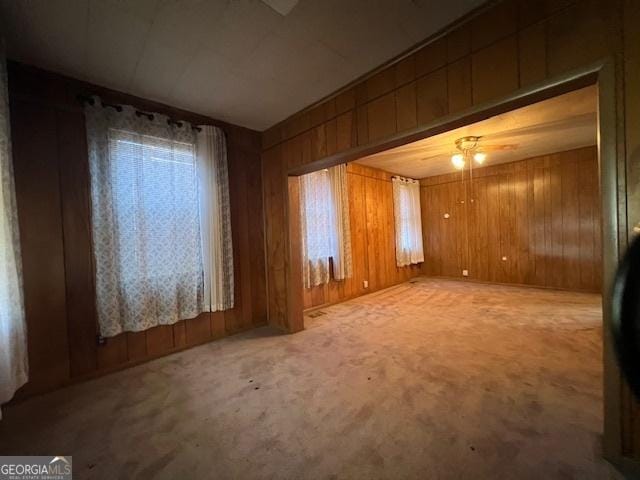 empty room featuring ceiling fan, carpet flooring, and wooden walls