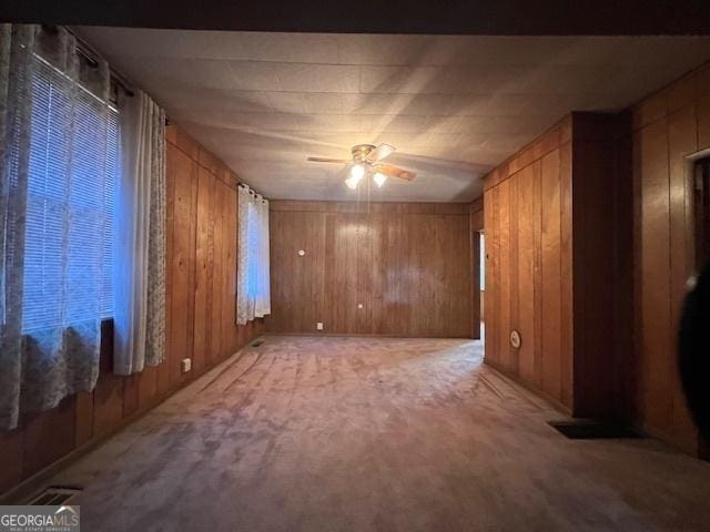 spare room with wooden walls, a ceiling fan, and light carpet