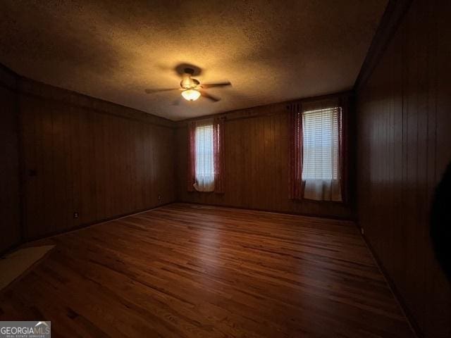 unfurnished room with wood walls, a ceiling fan, wood finished floors, and a textured ceiling
