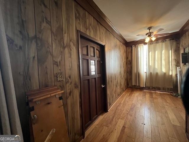 spare room featuring light wood-style floors, crown molding, wooden walls, and ceiling fan