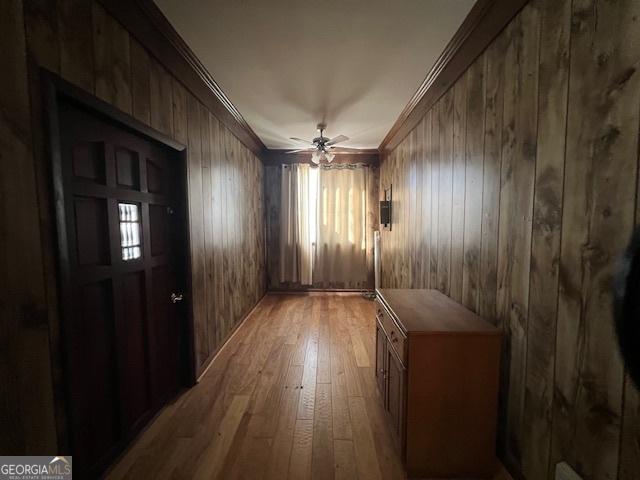 interior space with hardwood / wood-style flooring, wood walls, ornamental molding, and a ceiling fan