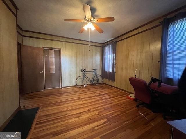unfurnished office featuring ornamental molding, a ceiling fan, wood finished floors, and wooden walls