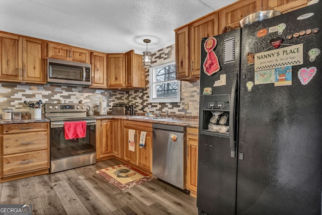 kitchen featuring appliances with stainless steel finishes, tasteful backsplash, hanging light fixtures, and wood-type flooring