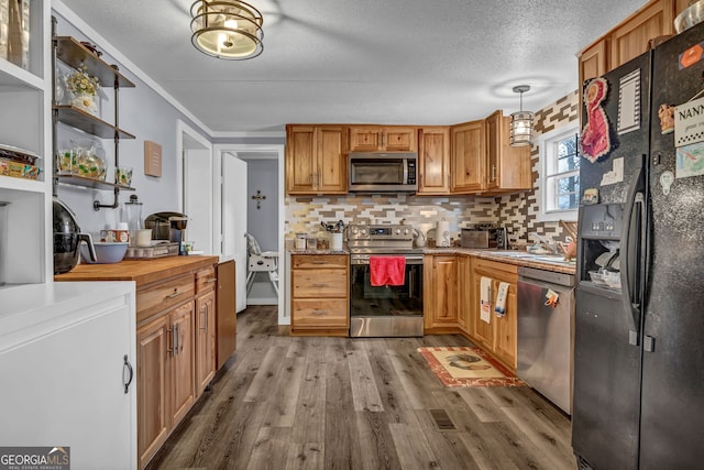 kitchen featuring decorative backsplash, light wood-type flooring, a textured ceiling, stainless steel appliances, and hanging light fixtures