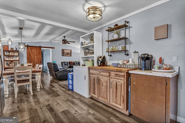 kitchen featuring vaulted ceiling, ceiling fan, pendant lighting, a barn door, and hardwood / wood-style floors