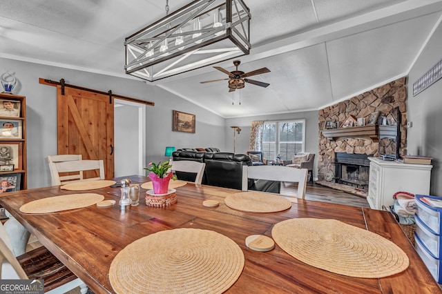 dining space featuring lofted ceiling, a stone fireplace, ceiling fan, a barn door, and wood-type flooring