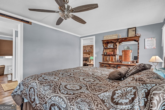 bedroom with ensuite bath, ornamental molding, ceiling fan, a barn door, and hardwood / wood-style flooring