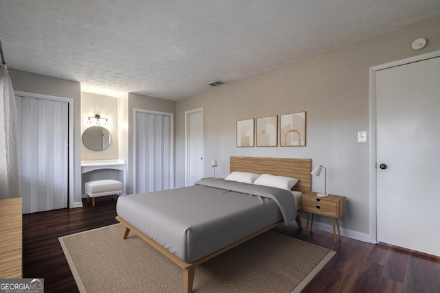 bedroom featuring a textured ceiling, multiple closets, and dark hardwood / wood-style floors