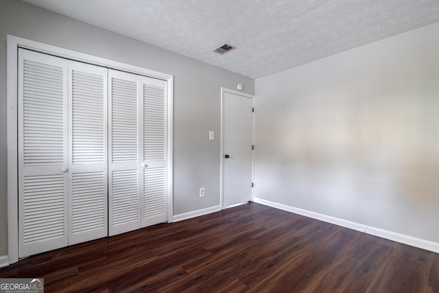 unfurnished bedroom with a textured ceiling, dark wood-type flooring, and a closet