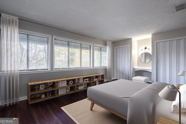 bedroom with a textured ceiling, dark hardwood / wood-style flooring, and multiple windows