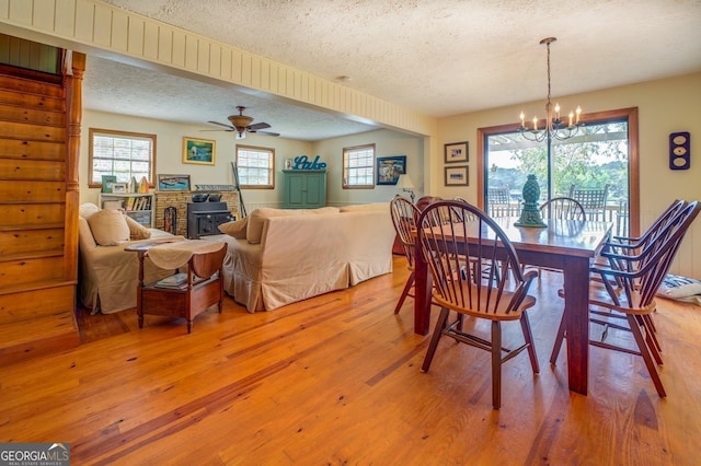 dining space featuring a wood stove, ceiling fan with notable chandelier, hardwood / wood-style flooring, a textured ceiling, and a healthy amount of sunlight