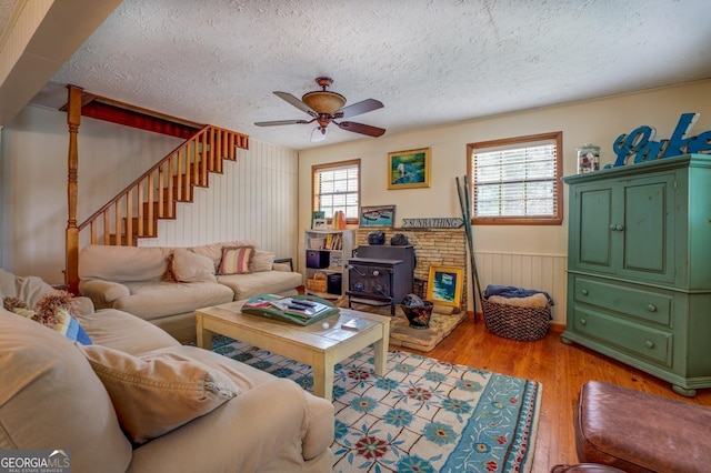 living room with ceiling fan, a wood stove, a textured ceiling, and light hardwood / wood-style flooring