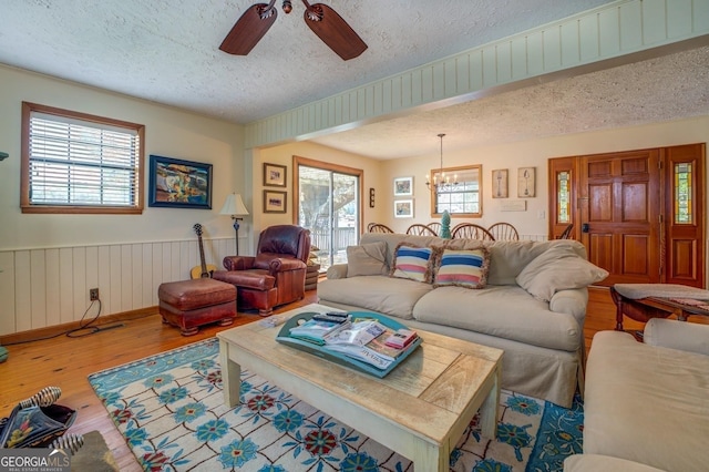 living room with hardwood / wood-style floors, ceiling fan with notable chandelier, and a textured ceiling