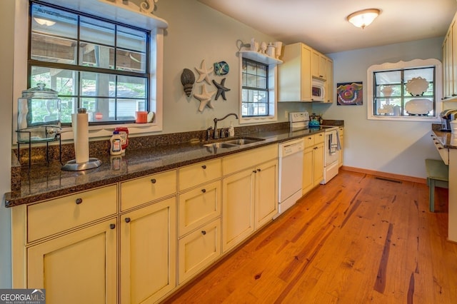 kitchen with sink, light hardwood / wood-style flooring, dark stone counters, white appliances, and cream cabinetry