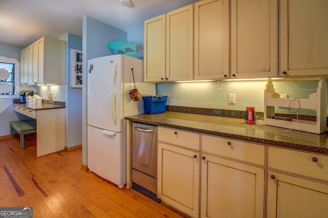 kitchen with stainless steel dishwasher, light hardwood / wood-style flooring, dark stone countertops, cream cabinetry, and white fridge