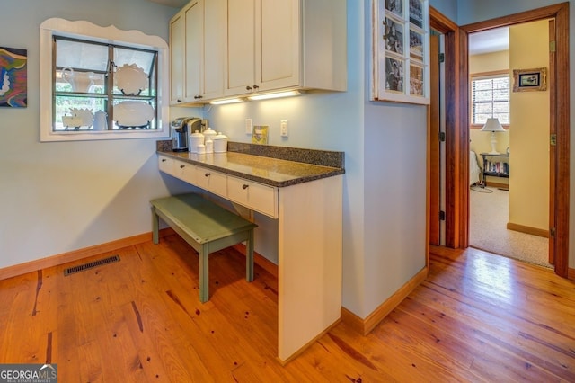 kitchen with dark stone countertops, white cabinetry, and light hardwood / wood-style flooring