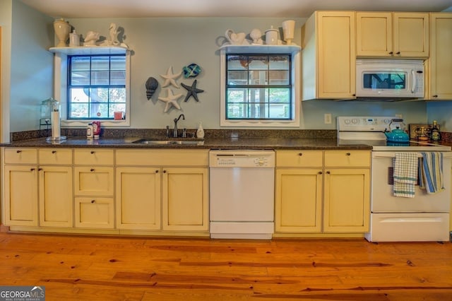 kitchen with dark stone countertops, white appliances, sink, and light hardwood / wood-style flooring