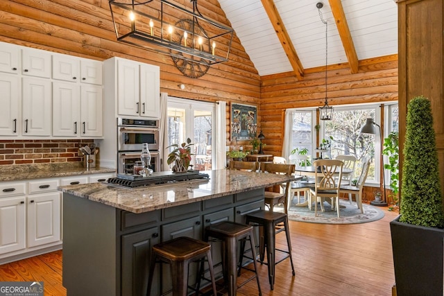 kitchen with light stone counters, log walls, pendant lighting, white cabinets, and a center island