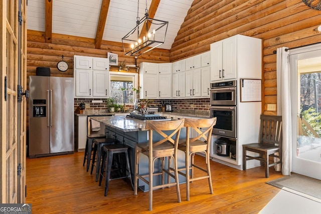 kitchen with appliances with stainless steel finishes, high vaulted ceiling, white cabinets, a kitchen island, and a breakfast bar area