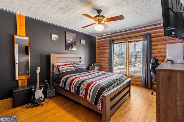 bedroom featuring ceiling fan, light wood-type flooring, a textured ceiling, and log walls